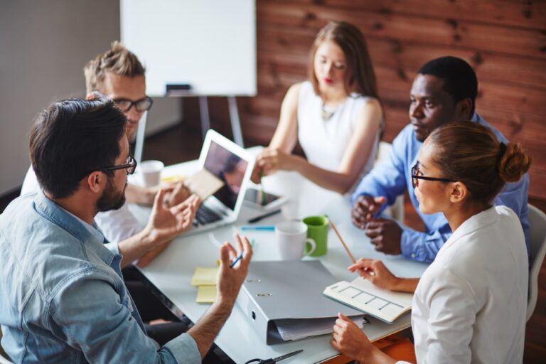 Groupe de professionnels en réunion de formation autour d’une table avec ordinateurs portables