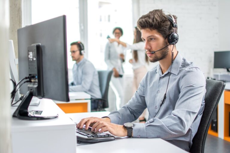 Technicien du support avec casque micro répondant à un client depuis son poste de travail